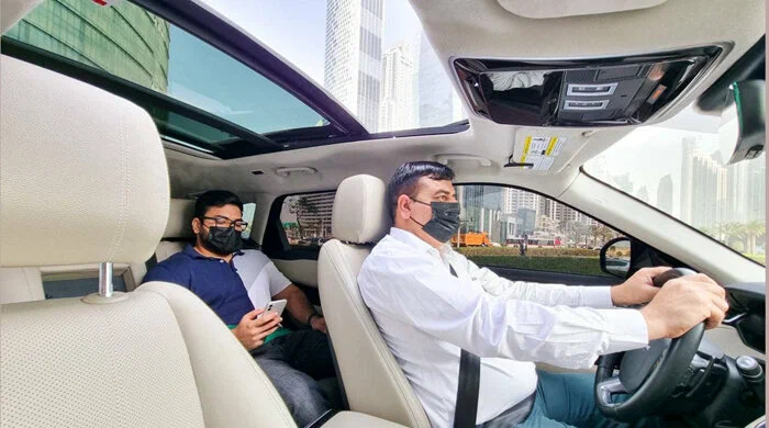 Driver and passenger wearing masks inside a car with city buildings outside