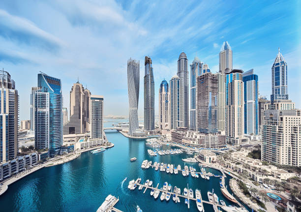 Dubai Marina skyline with modern skyscrapers, yachts, and waterfront view on a clear blue sky day.